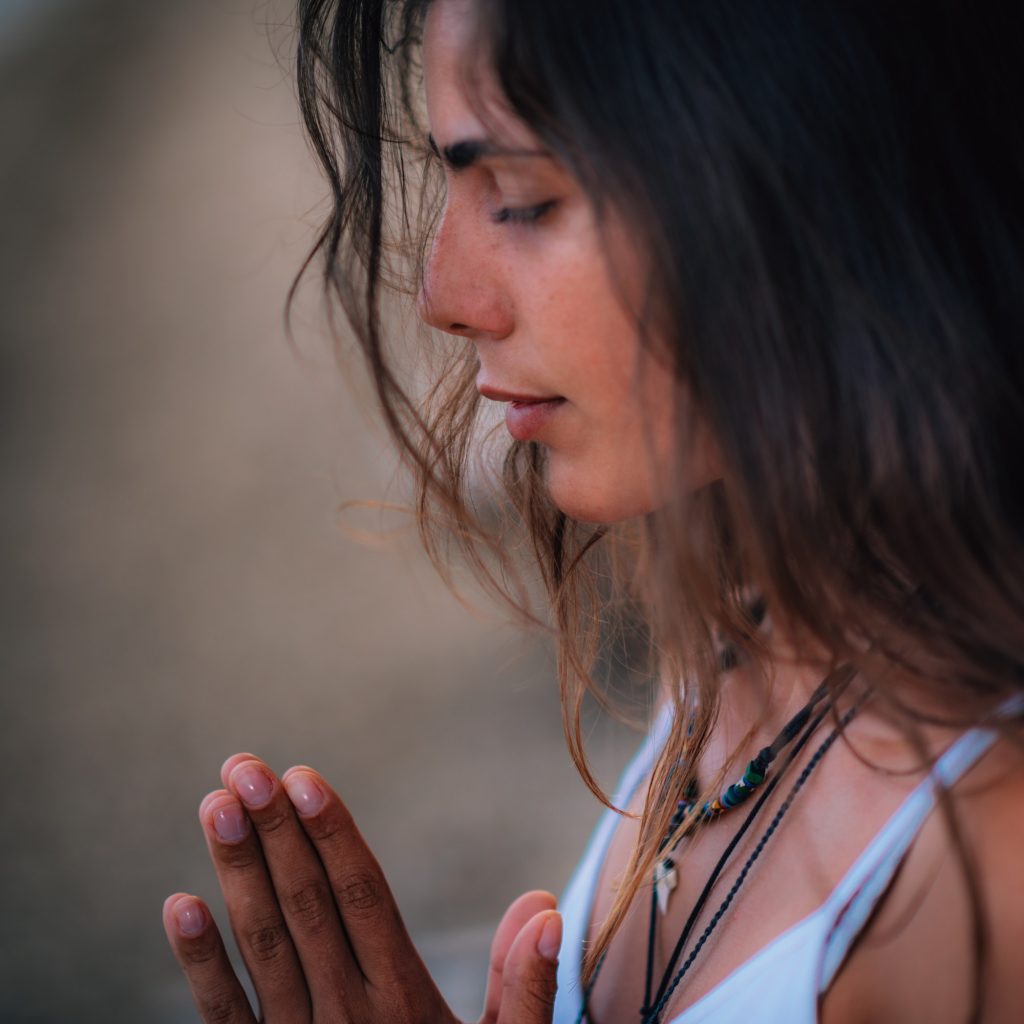 Young woman meditating with her eyes closed and hands together at heart level.