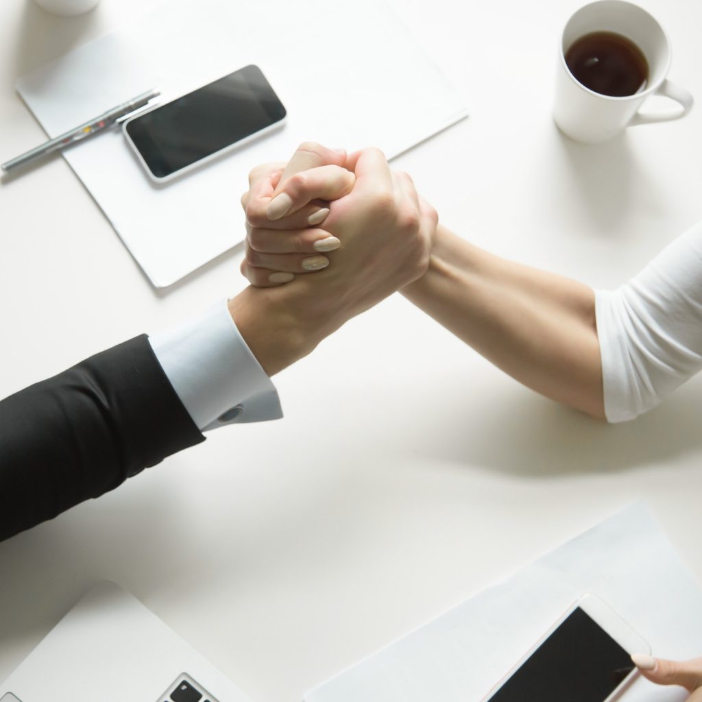 Close up of the arms of a businessman and a businesswoman arm-wrestling competitively to pin the other’s arm to the desk.